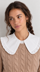 A woman wearing a beige cable-knit sweater with a contrasting white ruffled Peter Pan collar, shown in a close-up portrait against a light gray background.
