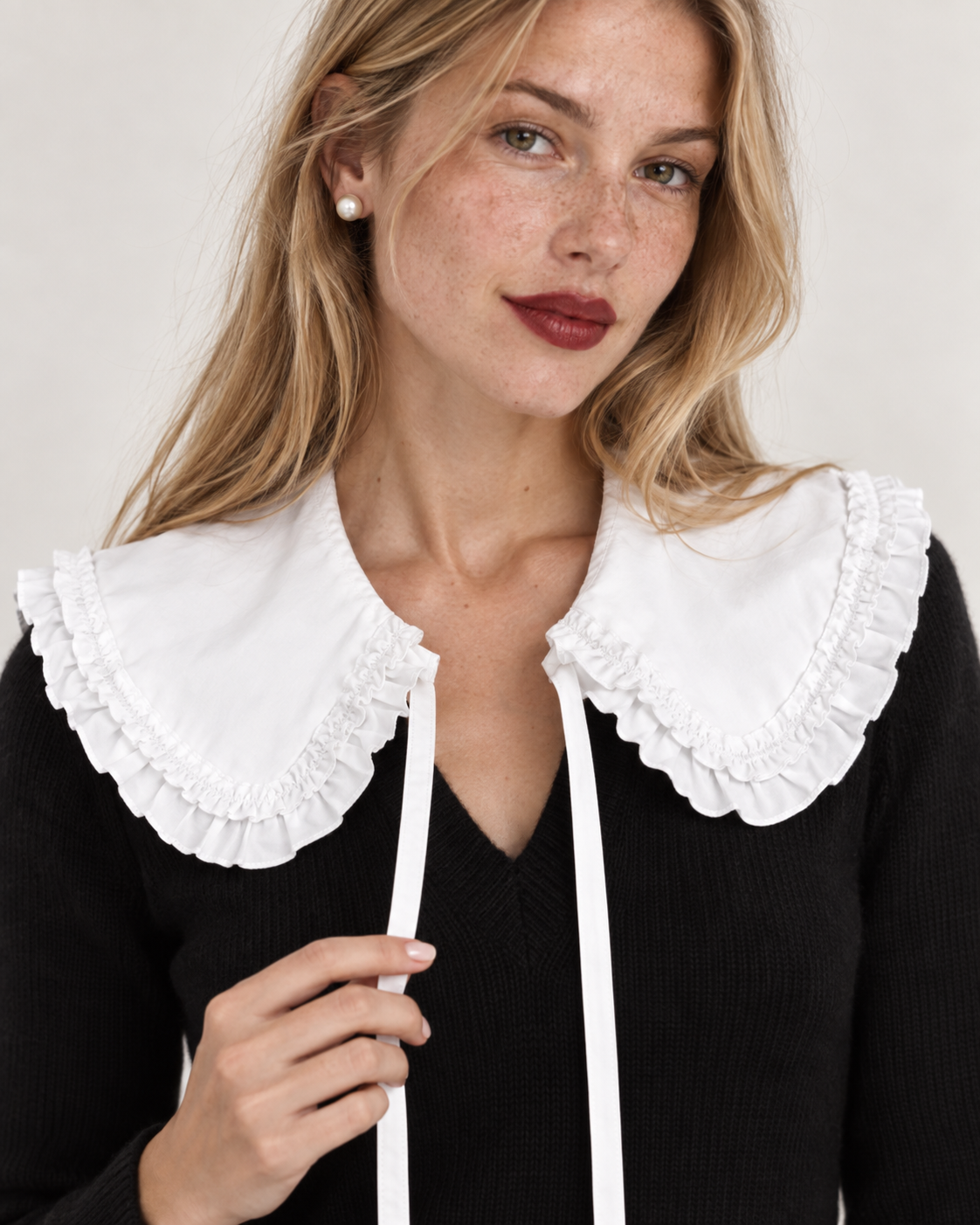 A close-up of a woman wearing a black knit sweater with a large white ruffled Peter Pan collar from the curated collar and white drawstrings.